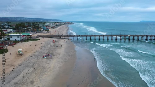 Drone flies low over beach and tourists walking in the sand towards pier
