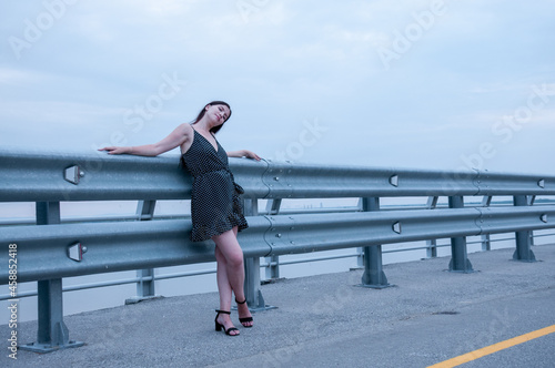 A girl with long hair in a black dress is standing near an empty road