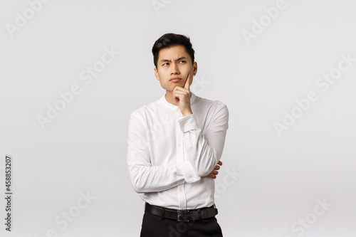 Handsome asian businessman trying understand meaning of life, touching chin, looking up with serious focused expression, thinking up business concepts, searching inspiration, pondering choices