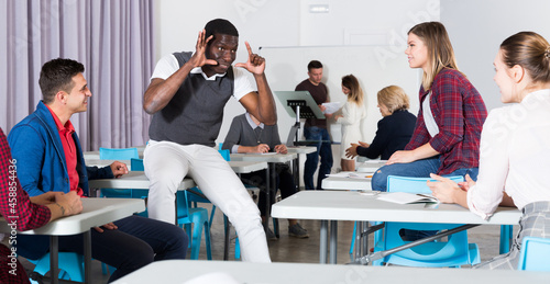 Friendly multinational group of students talking in classroom having break between lessons