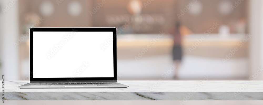 Fototapeta premium Laptop with blank white screen on marble table top with blurred luxury hotel lobby reception in the background.