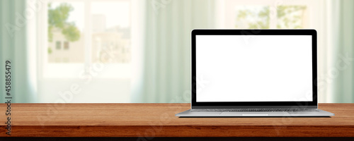 Laptop with blank white screen on wooden table and blurry image of Living room in background.