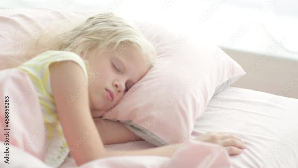 Adorable blonde girl sleeping sweetly in the morning on pink bed linens at home. Childrens dreams, comfort, rest and peace. Adorable blonde girl sleeping sweetly in the morning on pink bed linens at home. Childrens dreams, comfort, rest and peace.