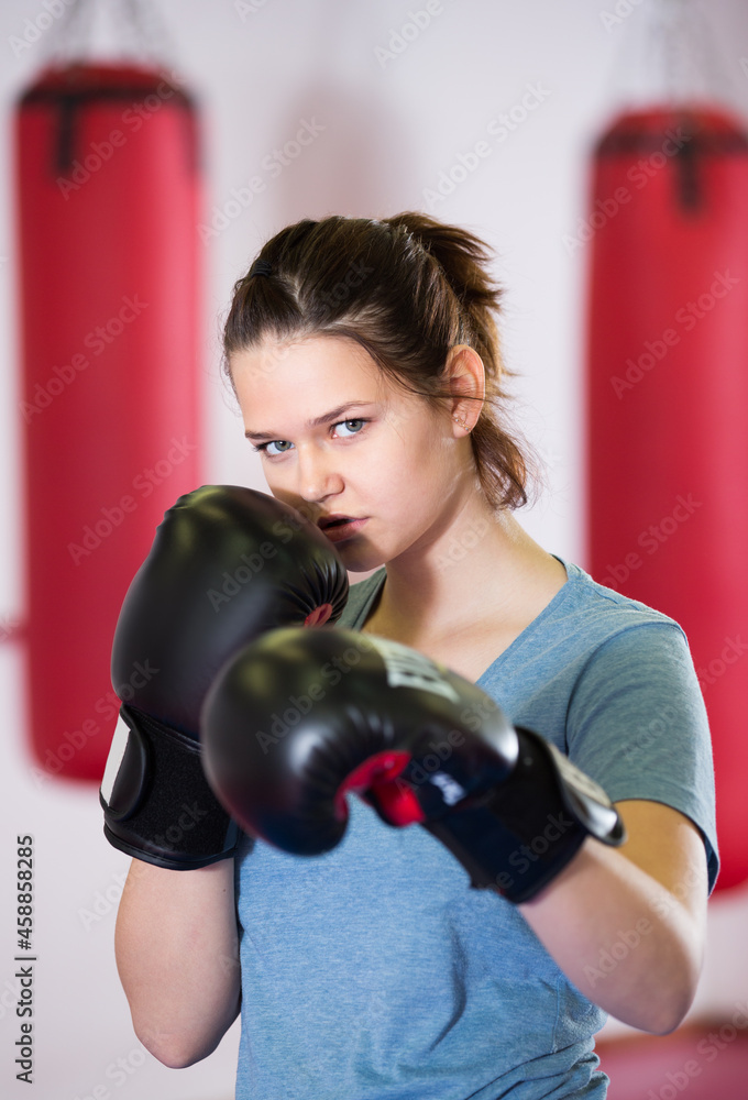 Portrait of young woman at gloves practicing different kiks in the boxing hall.