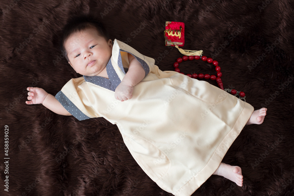 A cute Asian infant Muslim in thobe and rosary beads on red, muslim