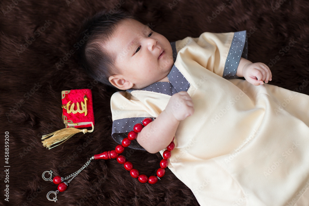A cute Asian infant Muslim in thobe and rosary beads on red, muslim