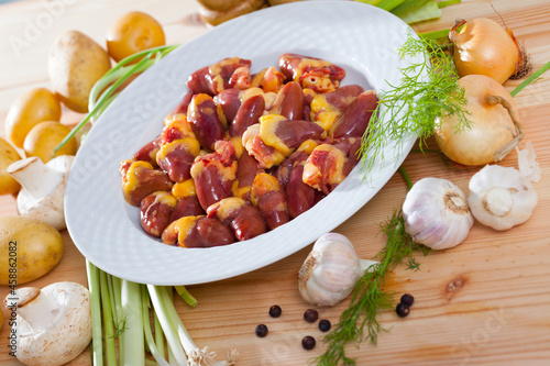 Ingredients for cooking. Fresh raw chicken hearts with potatoes, mushrooms, onion, garlic, spices on light wooden surface.. photo