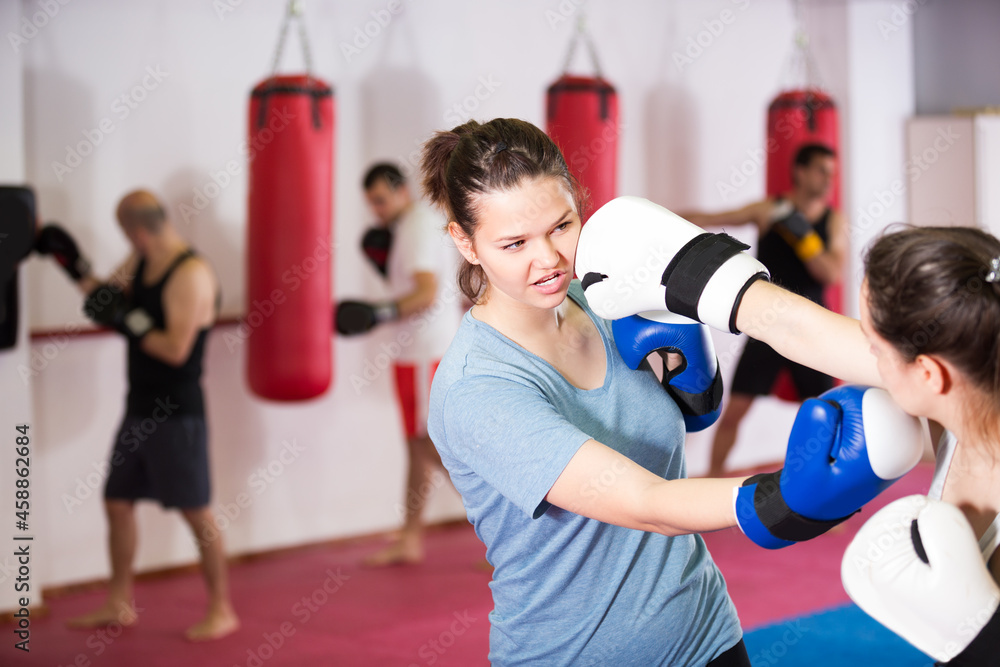 Young athlete female is having sparring with partner in the boxing hall.