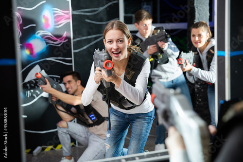 Excited girl aiming laser gun at other players during lasertag game in dark room..