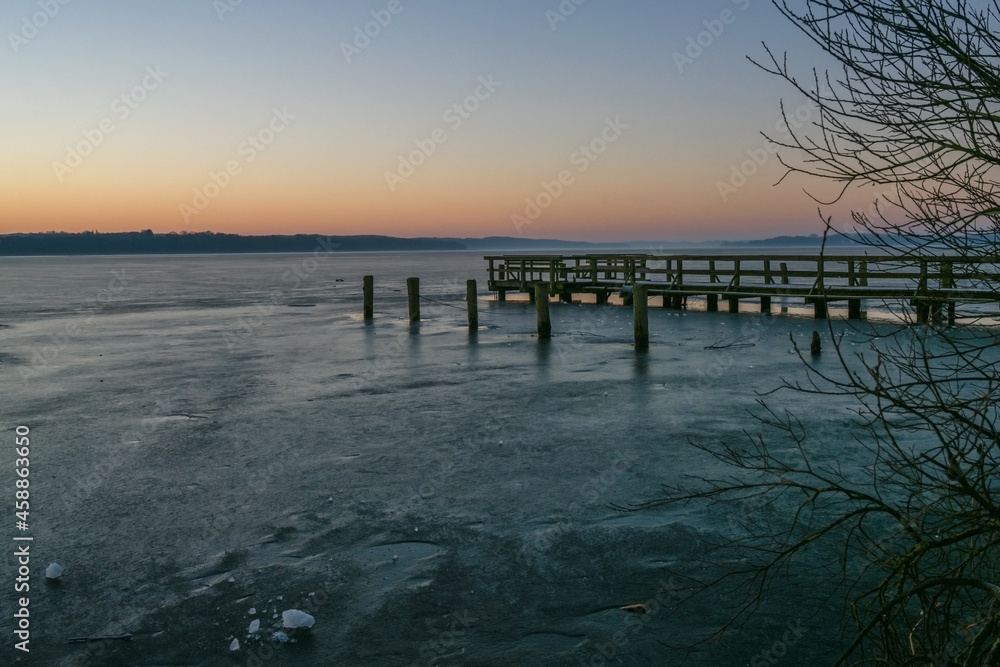 Wooden jetty and piles waiting for spring in a frozen lake on a cold day at dawn, tranquil landscape scenery, copy space