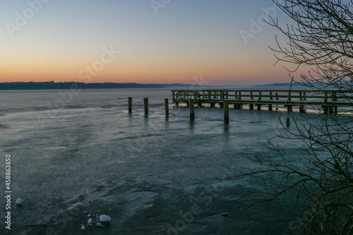 Wooden jetty and piles waiting for spring in a frozen lake on a cold day at dawn  tranquil landscape scenery  copy space