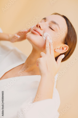 Young woman applying cosmetic white cream on face