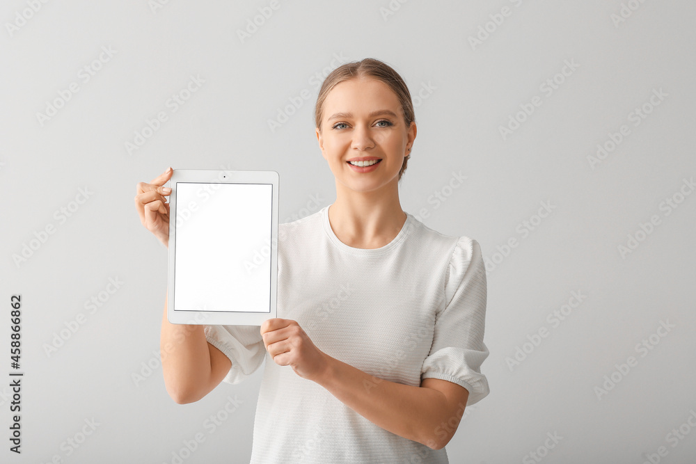 Beautiful young woman holding tablet computer with blank screen on grey background Beautiful young woman holding tablet computer with blank screen on grey background