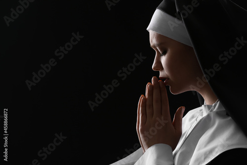 Young praying nun on dark b...