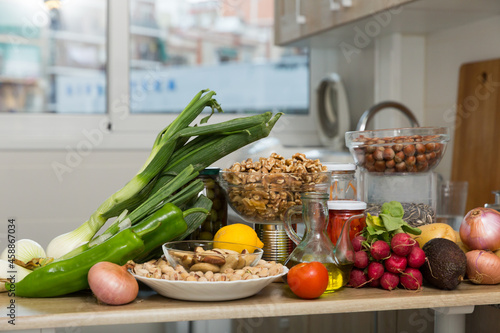 Variety of fresh vegetables, pickles in glass jars, nuts and decanter of oil on wooden kitchen tabletop. Vegetarian food concept photo