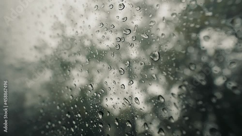 Rain water droplets on glass,  Large rain drops strike a window pane during a summer shower inCosta Rica Jungle. Nature and blurred trees in background photo