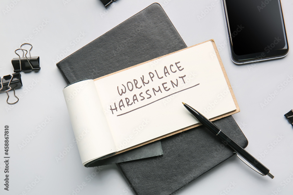 Notebook with text WORKPLACE HARASSMENT and mobile phone on light background Notebook with text WORKPLACE HARASSMENT and mobile phone on light background