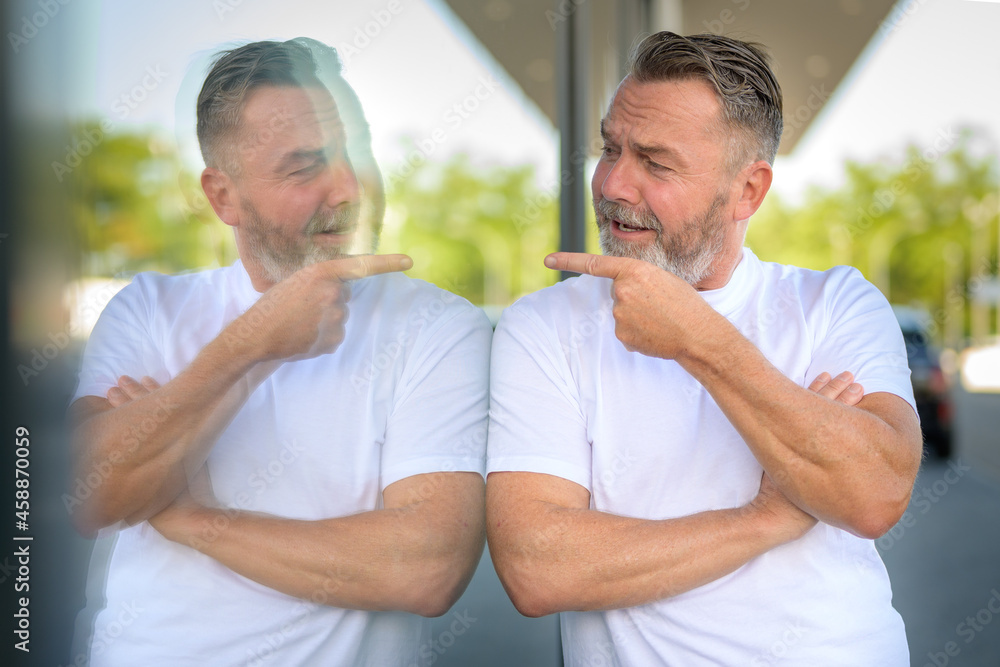 Fototapeta premium Playful man leaning against a window pointing at his reflection