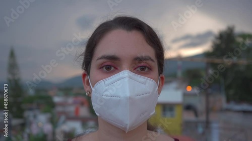 person with mask kn95. Young woman portrait with protective face mask looking at the camera with blurred city in the background photo