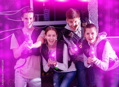 Happy young people with laser pistols posing together in bright beams in laser tag labyrinth. High quality photo