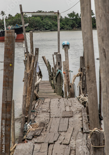 The old broken wooden pier by Chao Phraya River with cargo ship at the background.