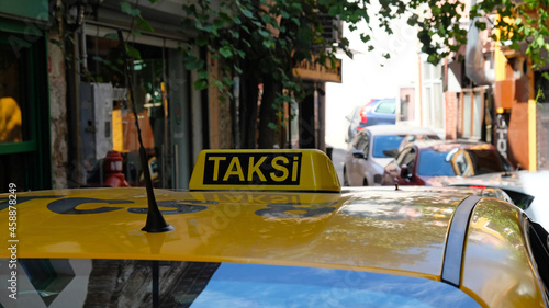 Yellow taxi in Istanbul, Turkey. Close up of a taxi sign. The word "taksi" translated from Turkish means "taxi". A yellow taxi drives down a narrow street in Istanbul.