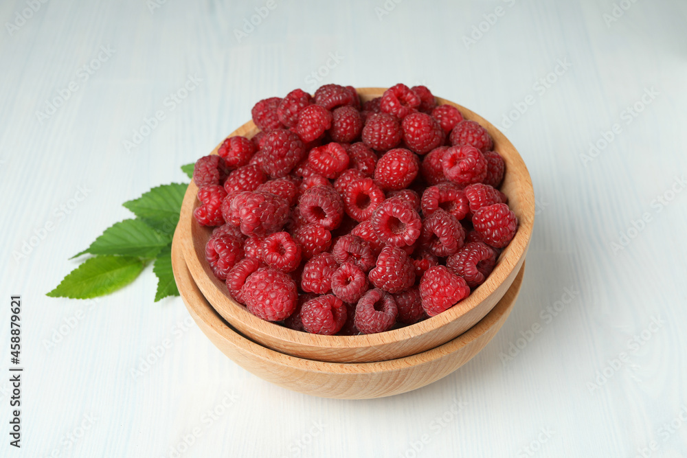 Red juicy raspberries in a wooden bowl on a white wooden background Red juicy raspberries in a wooden bowl on a white wooden background