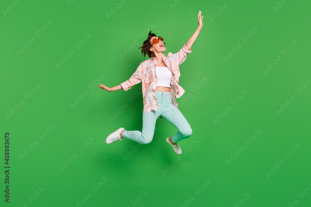 Full body photo of cheerful joyful happy woman jump up wear summer sunglass look empty space isolated on green color background Full body photo of cheerful joyful happy woman jump up wear summer sunglass look empty space isolated on green color background