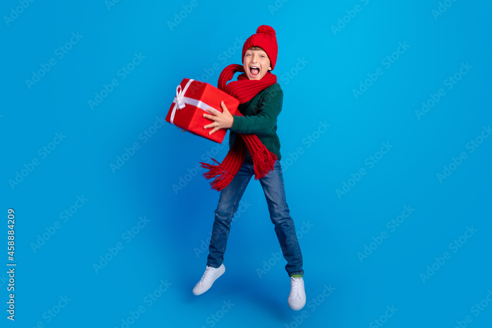 Full length body size photo boy jumping keeping xmas present isolated bright blue color background Full length body size photo boy jumping keeping xmas present isolated bright blue color background
