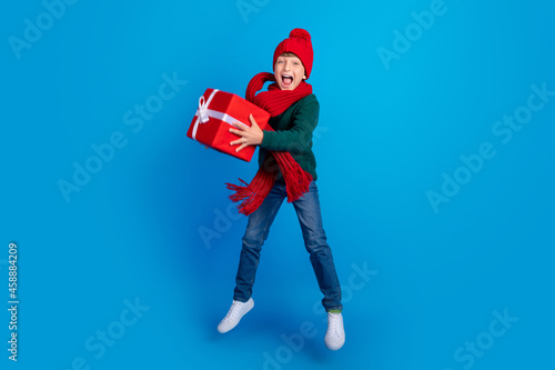 Full length body size photo boy jumping keeping xmas present isolated bright blue color background