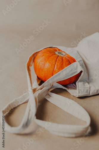 Orange pumpkin in beige shopper on paper background. Halloween pumpkin inside beige bag.