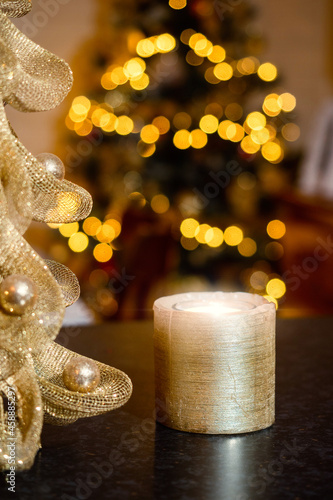 Small candle burning in foreground. Christmas decorated tree in the background. Selective focus. Festive season theme. Dark and moody atmosphere.