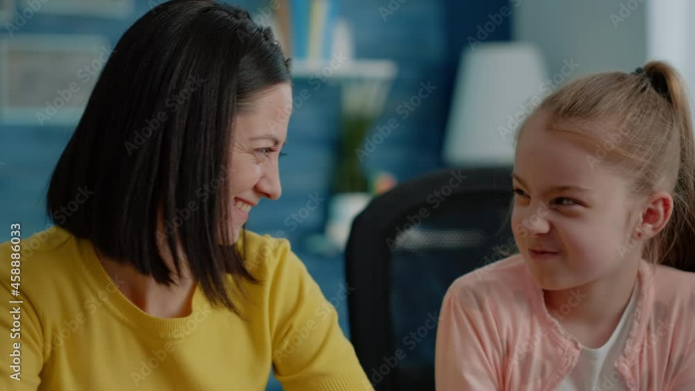 Close up of schoolgirl and mother doing homework together at desk. Portrait of parent and daughter preparing for online remote classes, looking at camera. Primary school pupil and adult Close up of schoolgirl and mother doing homework together at desk. Portrait of parent and daughter preparing for online remote classes, looking at camera. Primary school pupil and adult