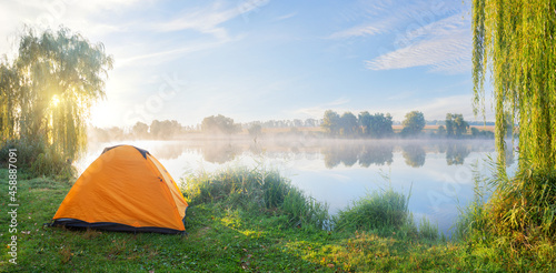 Foggy lake shore with orange tent in morning sun