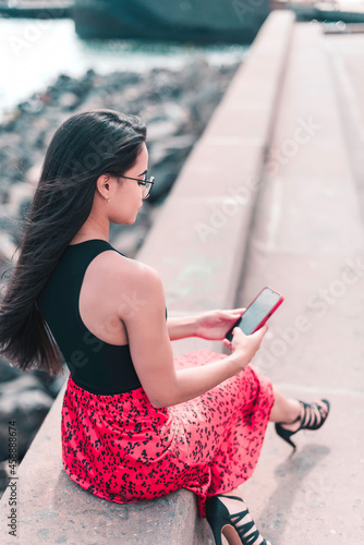 Young long hair woman is sitting on a bank and looking down to her mobile phone. Connecting people concept 