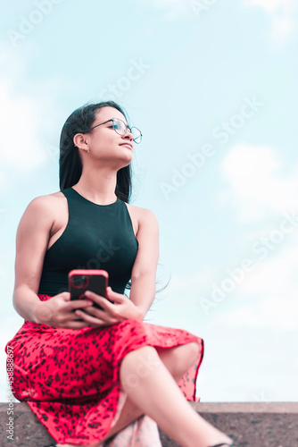 Woman is sitting on the street holding her mobile phone in the hands and looking forward. Connecting people concept 