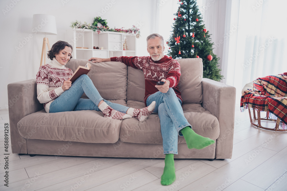Full length photo of nice couple old lady man sit watch tv wear sweater jeans socks at home Full length photo of nice couple old lady man sit watch tv wear sweater jeans socks at home