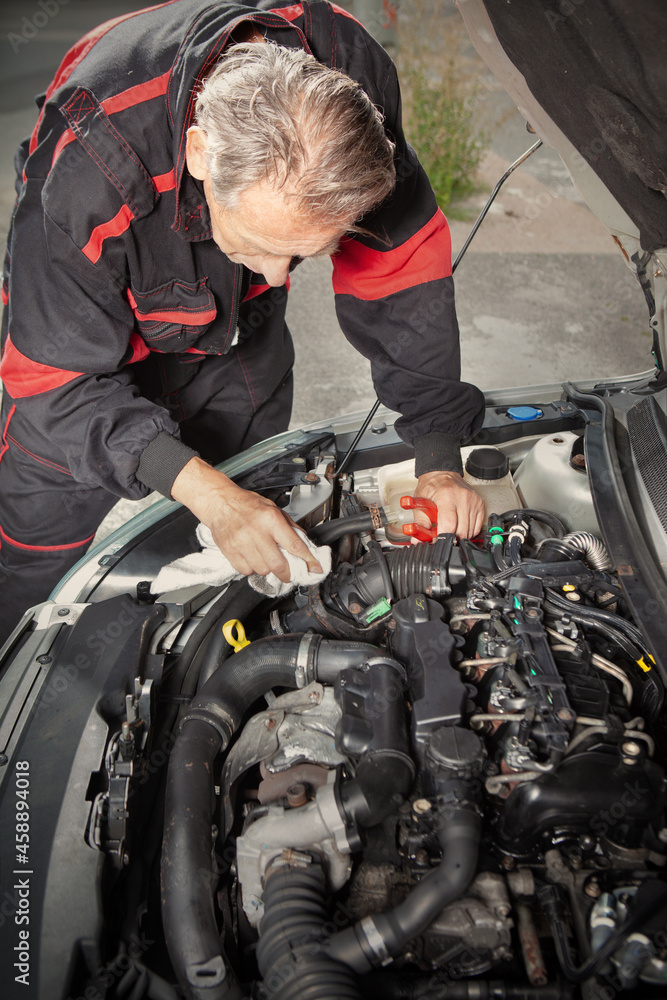 Man in overall working on open engine of his car directly on street Man in overall working on open engine of his car directly on street