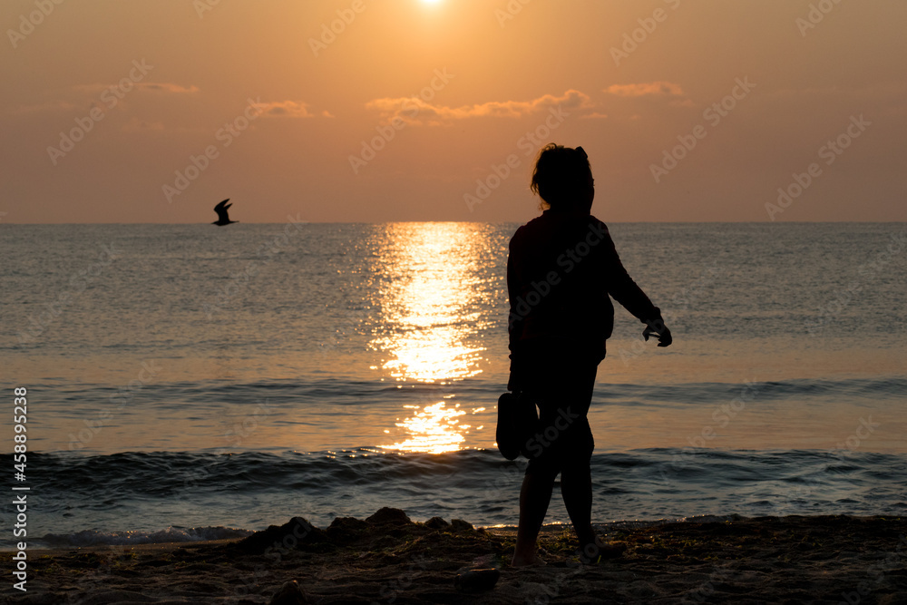 A woman (silhouette) walks alone on the beach in the early hours of the morning, when the sun rises. Beautiful sunrises and sunsets. 