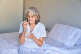 Kranke Seniorin sitzt auf dem Bett und nimmt eine Tablette ein