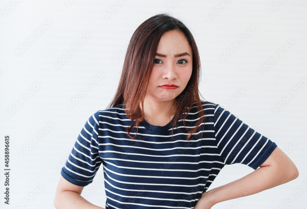 Studio portrait shot of Asian young angry mad crazy grumpy upset serious stress aggressive sad female model in casual clothing staring look at camera posing holding hand on waist on white background Studio portrait shot of Asian young angry mad crazy grumpy upset serious stress aggressive sad female model in casual clothing staring look at camera posing holding hand on waist on white background