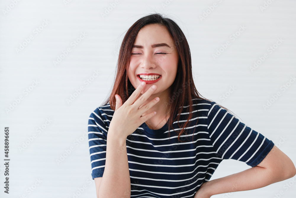 Studio portrait shot of Asian young happy charming cheerful joyful female model wears casual clothing closing eyes smiling laughing holding fingers on chin and hand on waist on white background Studio portrait shot of Asian young happy charming cheerful joyful female model wears casual clothing closing eyes smiling laughing holding fingers on chin and hand on waist on white background