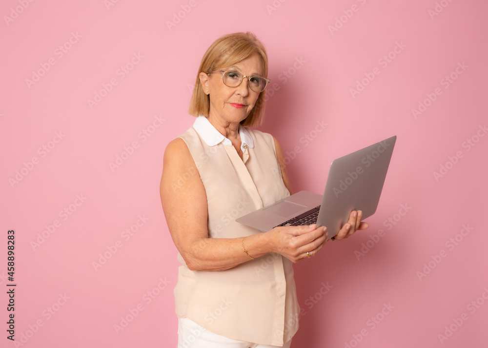 Cheerful mature woman using laptop computer standing isolated over pink background Cheerful mature woman using laptop computer standing isolated over pink background
