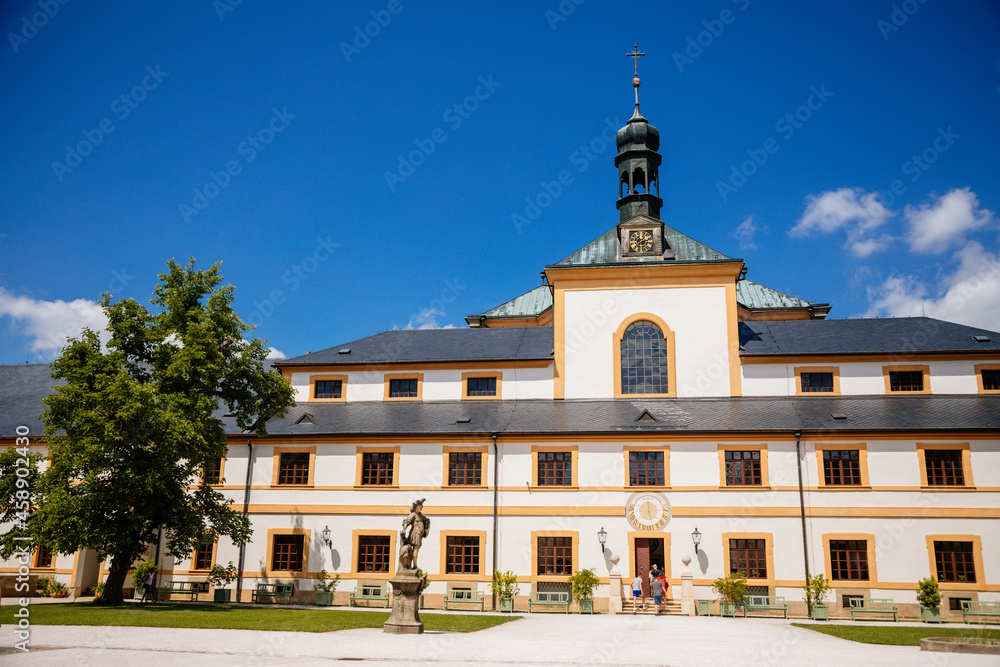 Kuks, East Bohemia, Czech Republic, 10 July 2021: Baroque castle and hospital Kuks, courtyard with antique sundial on the facade, Beautiful complex with chateau and Holy Trinity Church at summer day.