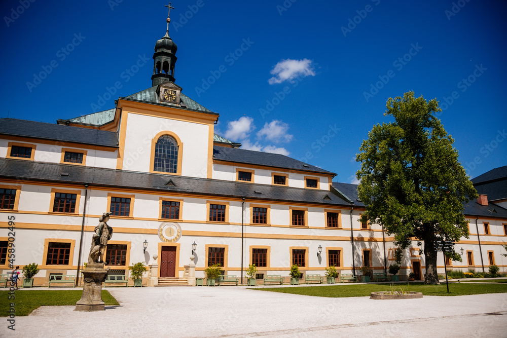Kuks, East Bohemia, Czech Republic, 10 July 2021: Baroque castle and hospital Kuks, courtyard with antique sundial on the facade, Beautiful complex with chateau and Holy Trinity Church at summer day.