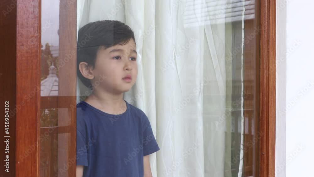 Sad little boy standing behind the window. Can't go outside. Unhappy asian preschooler Sad little boy standing behind the window. Can't go outside. Unhappy asian preschooler