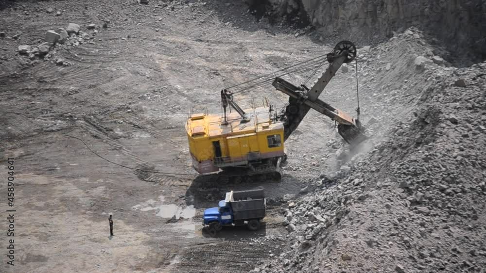 Large industrial excavator works in granite quarry stones and loads in truck Large industrial excavator works in granite quarry stones and loads in truck
