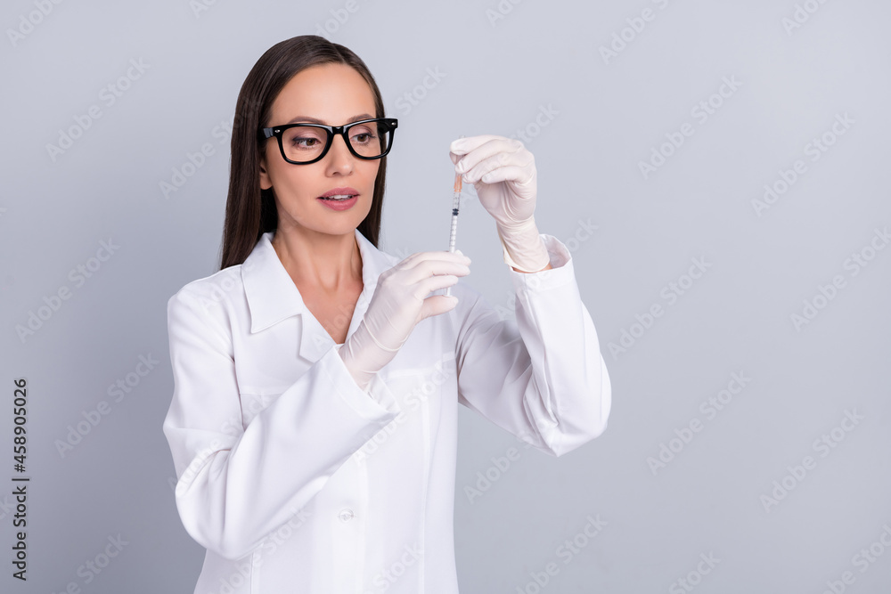 Portrait of attractive smart clever doctor preparing injection vaccine isolated over grey pastel color background Portrait of attractive smart clever doctor preparing injection vaccine isolated over grey pastel color background