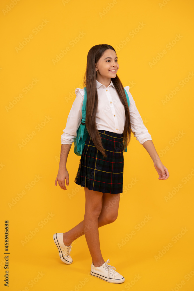 happy teen girl in school uniform full length on yellow background making step forward, school. happy teen girl in school uniform full length on yellow background making step forward, school.