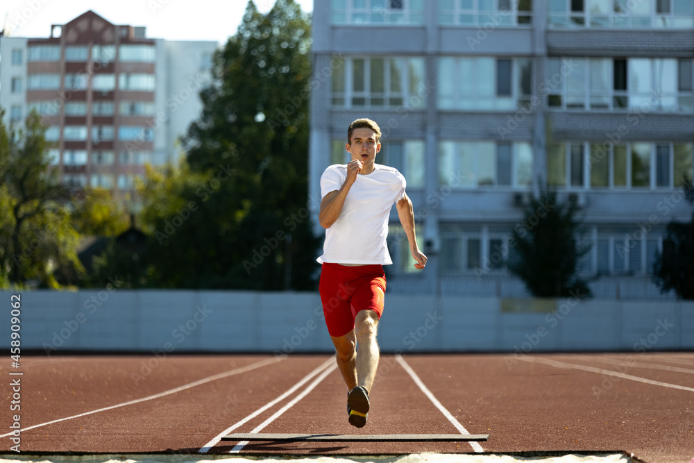 Young Caucasian man, male athlete, runner practicing alone at public stadium, sport court or running track outdoors. Summer sport games.